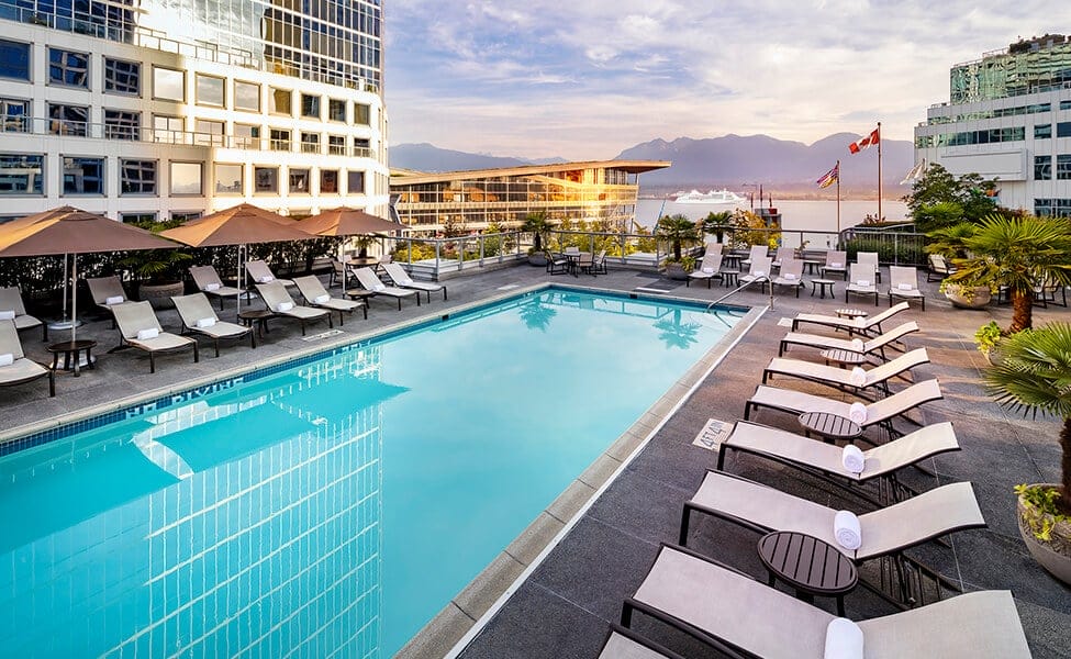 Hotel pool lined by lounge chairs with view of mountains, ocean and cruise ship in background