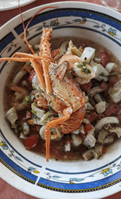 Closeup of white bowl with blue rim with small flowers. A stew with seafood with a large langoustine on the top