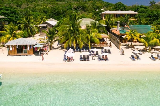Aerial view of beach club with chairs and cabanas on the edge of clear turquoise water and white sand beach.