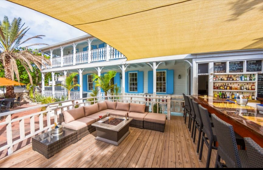 Large covered patio with outdoor bar, couch seating, with table seating down a few stairs to the left. Looks to be inside the courtyard of the inn.