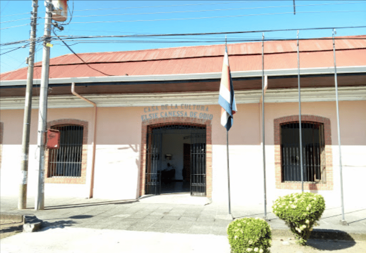 1 floor pink building with open arched doorway with "Casa de la Cultura" written above.