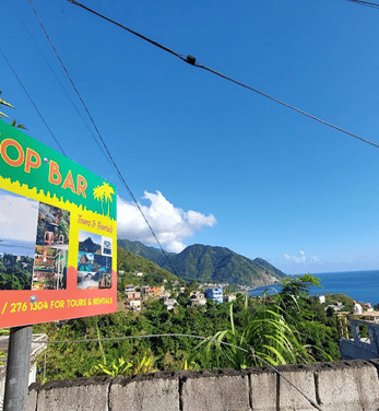 View of Roseau from hilltop with mountain in background and sign in the foreground left for "Top Bar"