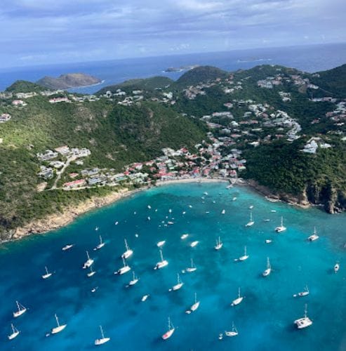 Corossol St. Barth, from the airplane. The village is huddled around a small beach and bay filled with boats. In the distance there are hills and the ocean on the other side of the island.