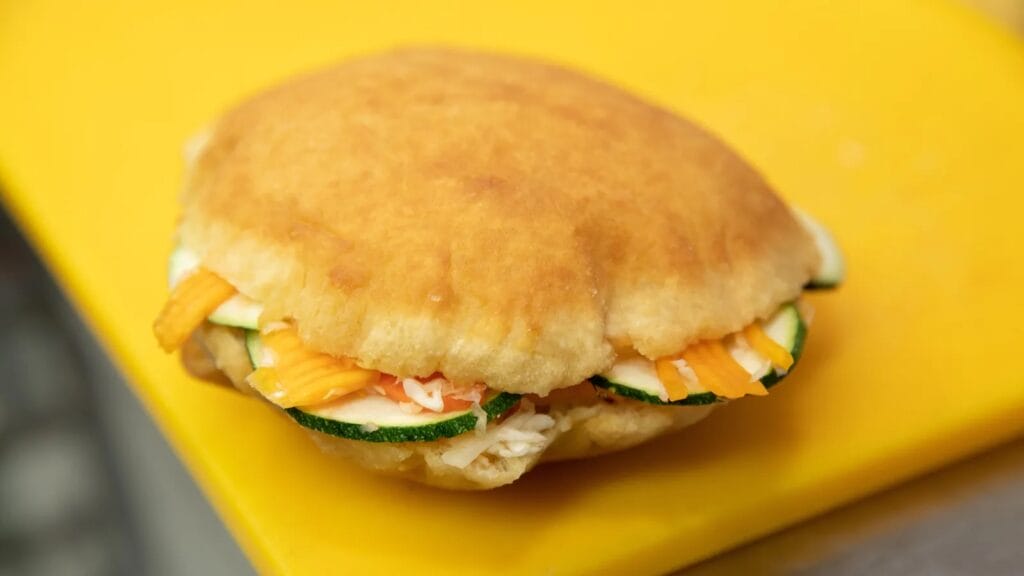 Small sandwich on a fried bun. Cucumber, cheese and meat are sticking out of the bun. 