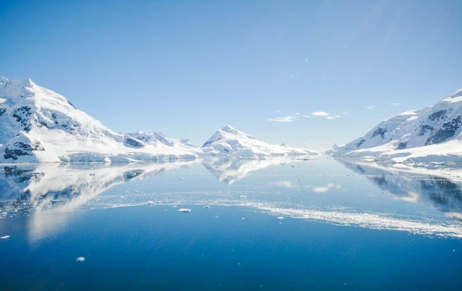 A lake in the Antarctic with large chunks of ice in the water and snow covered mountains in the background.