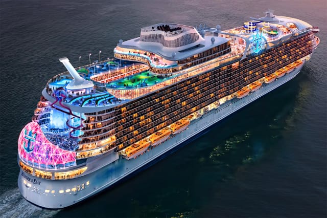 A cruise ship on the open water and colorful lights on all decks