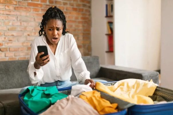 woman looking at her phone with a shocked look on her face while packing her suitcase