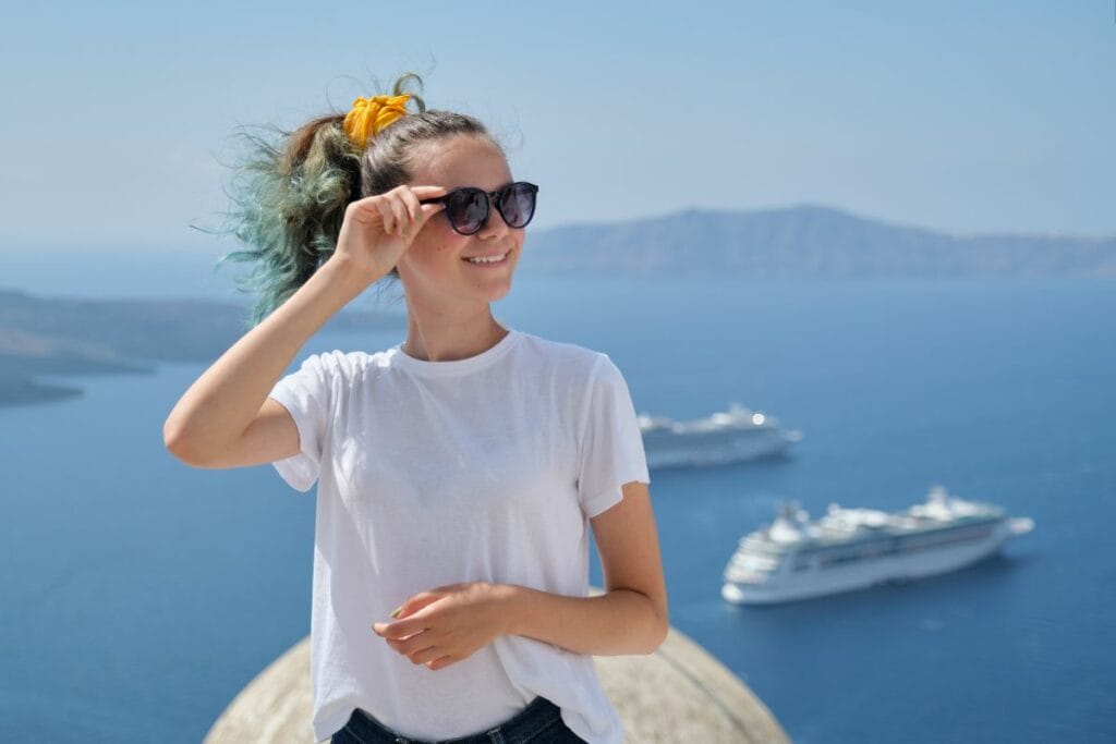 A young woman with sun glasses and smiling with two cruise ships in the background