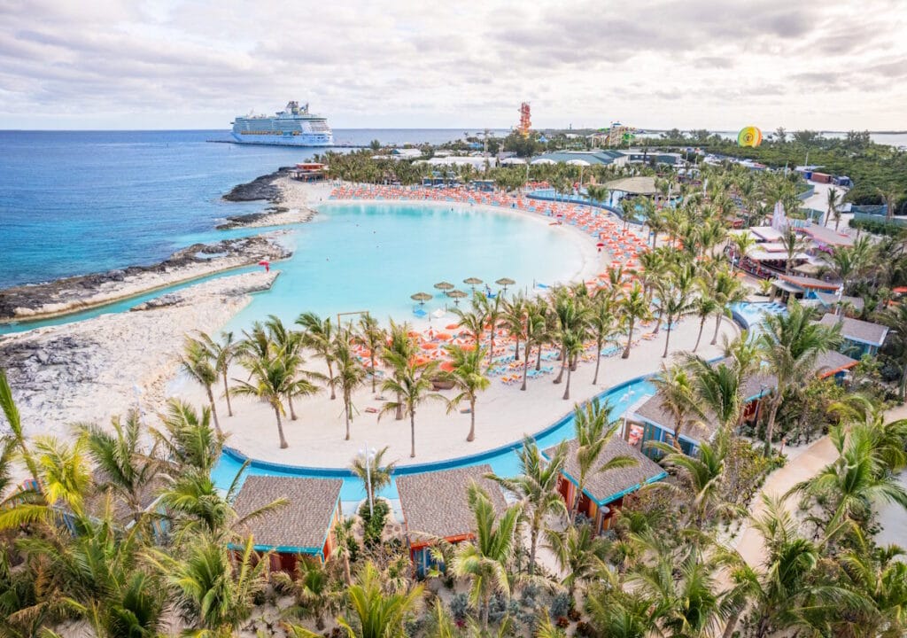 Cococay picture of a beach with palm trees and umbrellas and a cruise ship at the dock